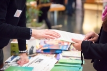Close up image of people exchanging informational materials over a table of brochures